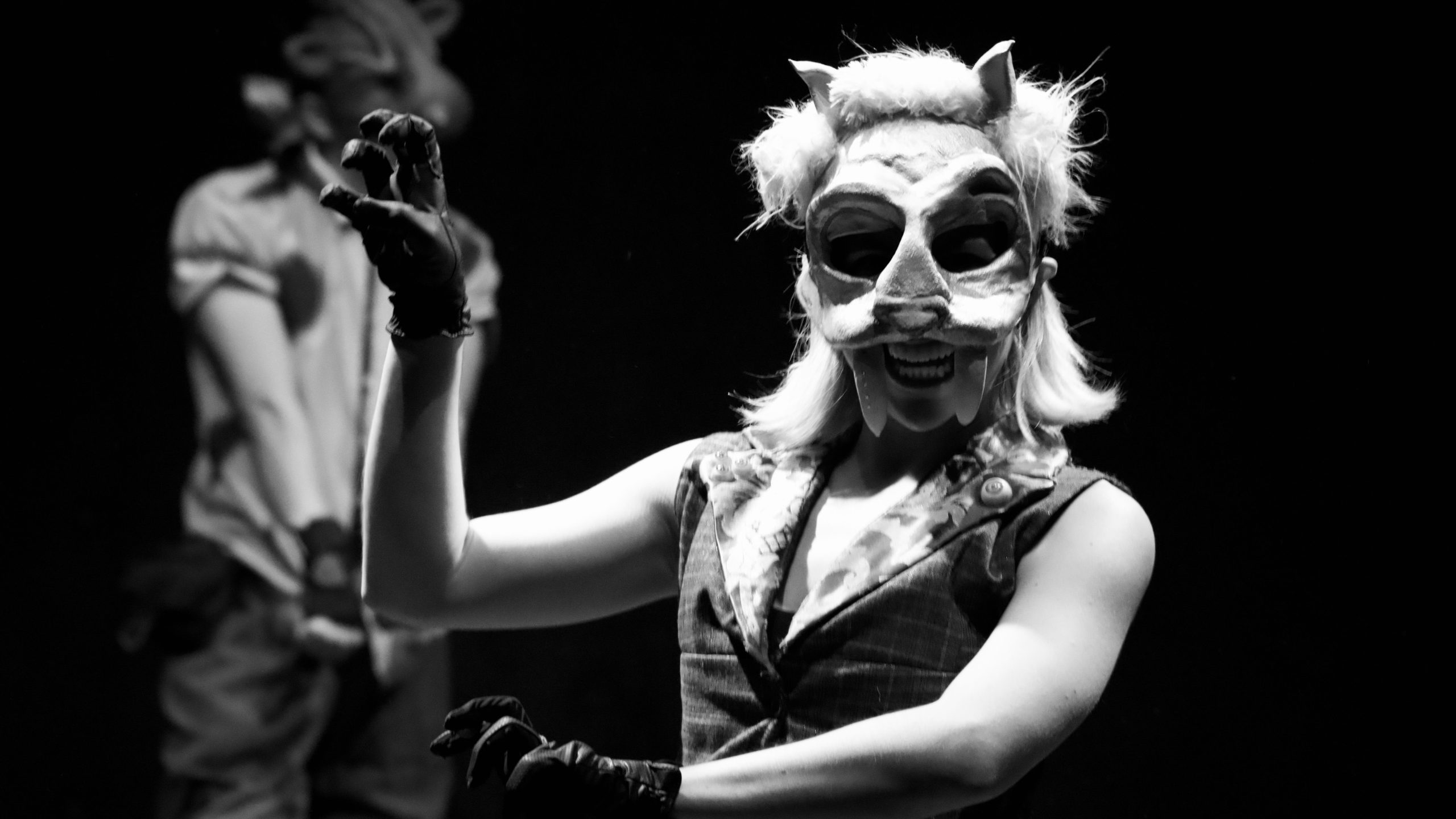 A woman wearing a mask and gloves stands on stage, possibly presenting on the topic of human-animal hybrids.